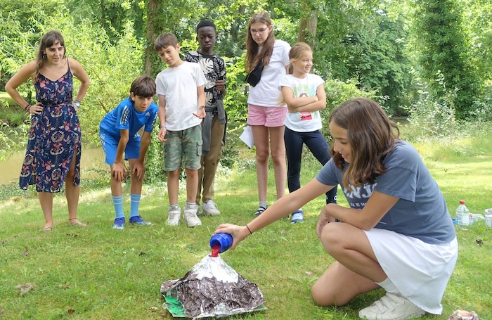 Children watch an outdoor volcano experiment during a hands-on English summer camp activity.