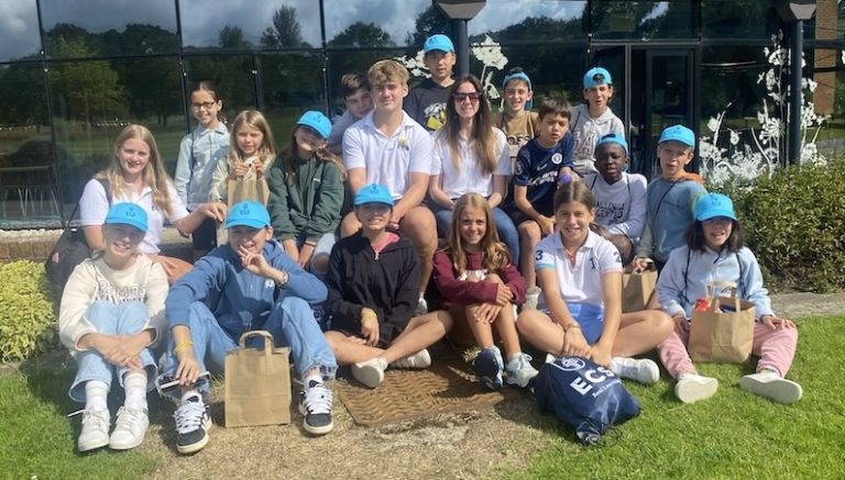 Young learners in blue caps gather outdoors during an English Country Schools summer camp.